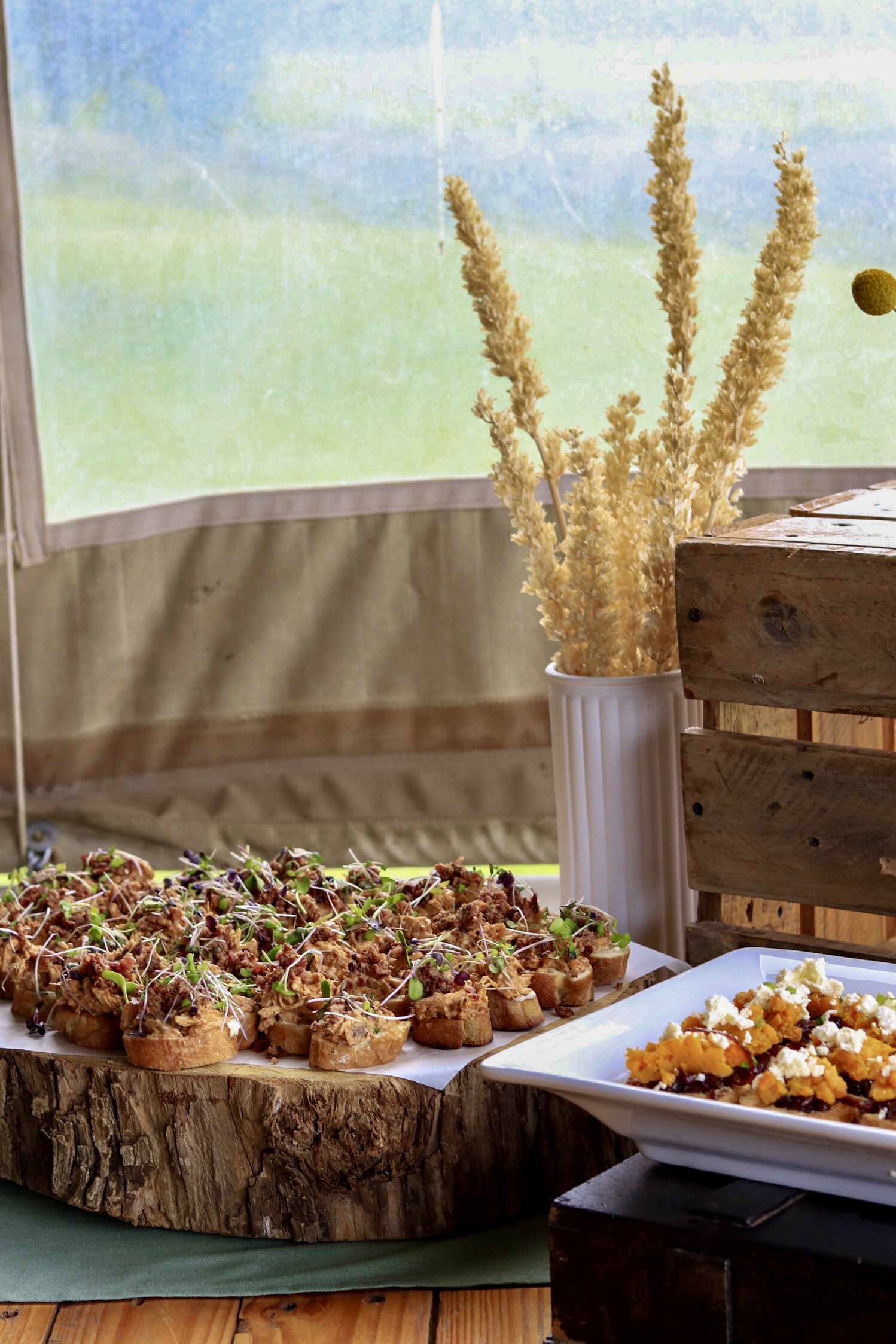 A spread of canapés on a wooden board at an outdoor catering setup.