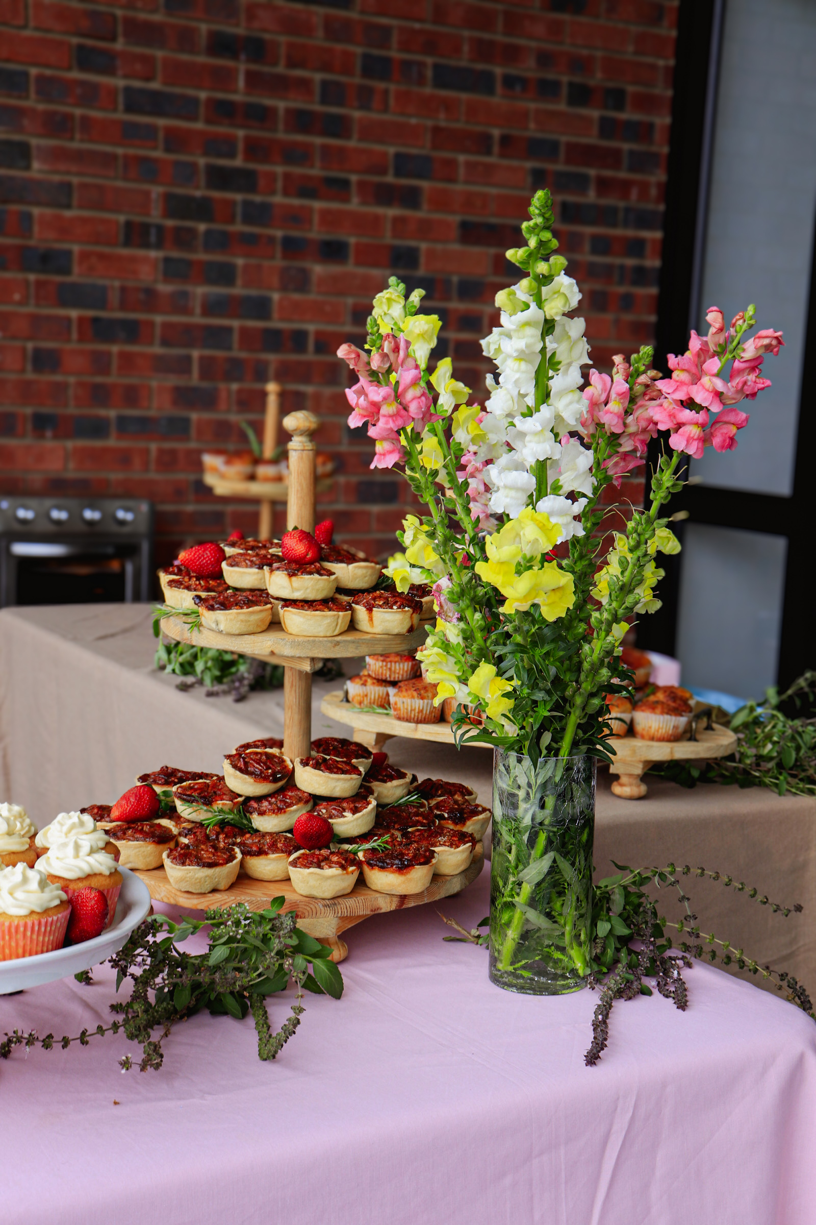A dessert table with tarts and cupcakes beside a vase of snapdragons.