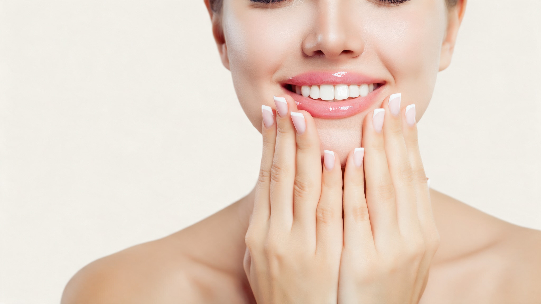 A woman with a soft French manicure smiling, her fingertips resting at her chin.