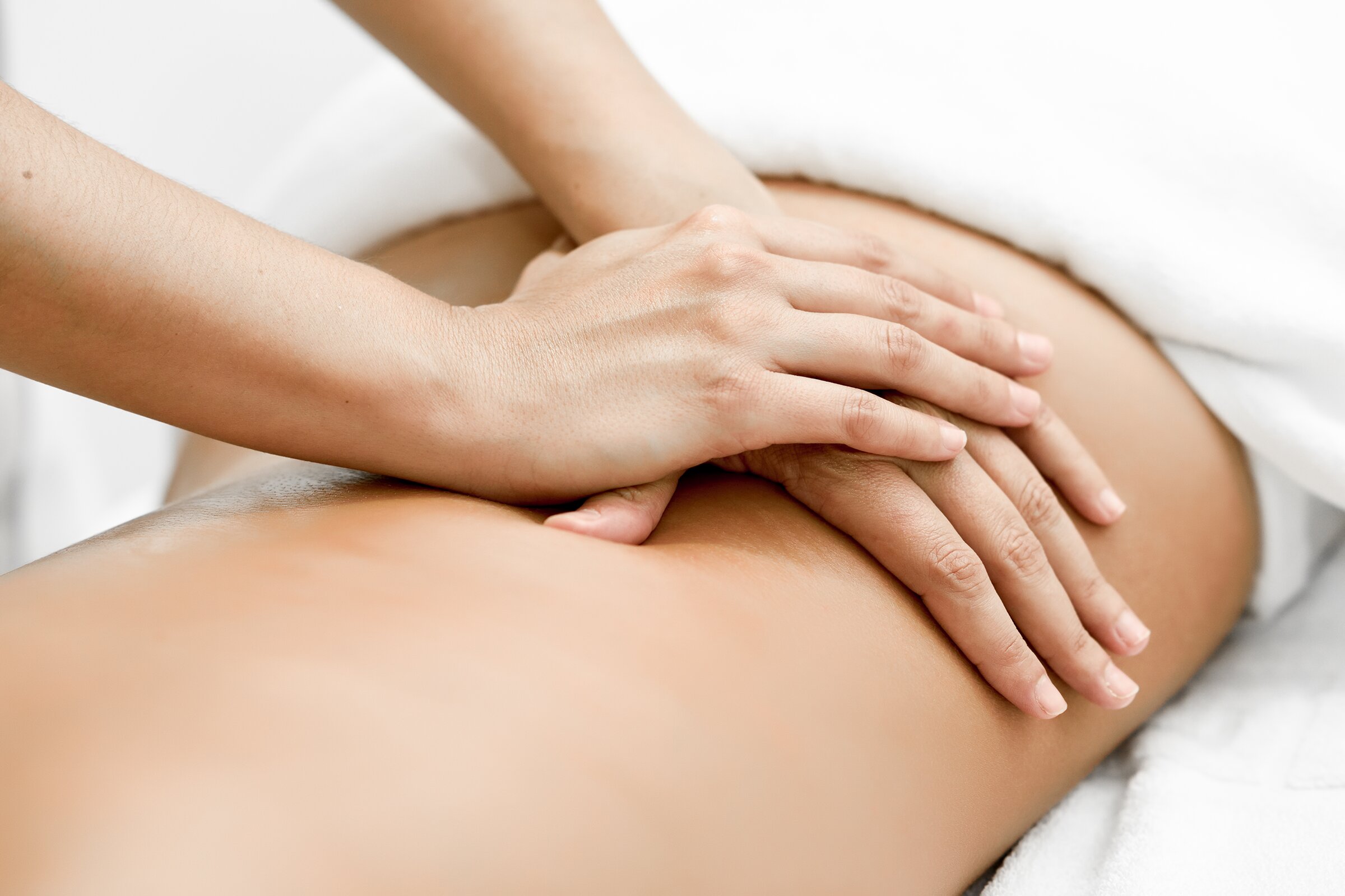 Two hands pressing down along a bare back, with white towels folded either side.
