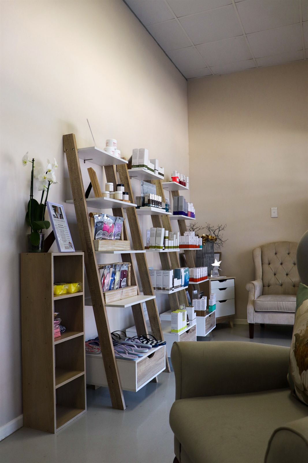 A leaning ladder shelf of boxed and bottled products in the salon’s retail corner, beside a white orchid and an armchair.