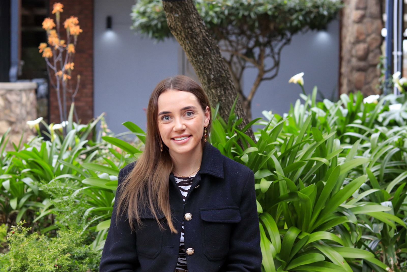The owner of Sarah & Co. standing outside the salon, in front of green garden planting.